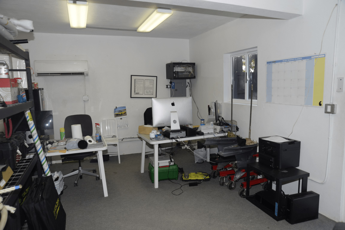 Maintenance area office cluttered workspace with desks computer equipment shelves and a
