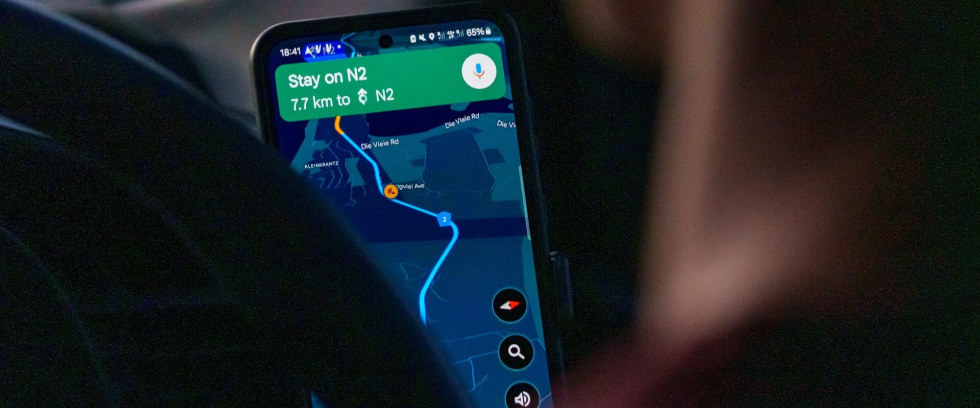 A smartphone mounted inside a car showing a Google Maps navigation route, the next instruction reading Stay on N2.
