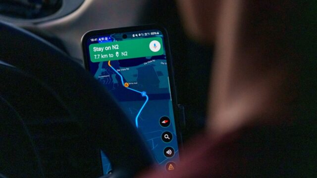 A smartphone mounted inside a car showing a Google Maps navigation route, the next instruction reading Stay on N2.